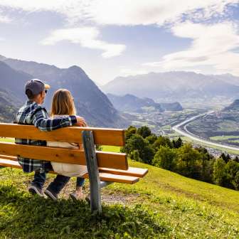 Couple assis sur un banc à Triesenberg et regardant la vallée du Rhin au Liechtenstein avec un panorama alpin impressionnant