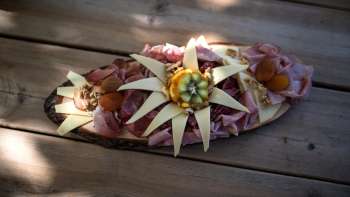 Une planche de bois artistiquement disposée avec différentes sortes de saucisses, du fromage et une décoration de fleurs comestibles, servie sur une table en bois. Une planche de bois artistiquement disposée avec différentes sortes de saucisses, du fromage et une décoration de fleurs comestibles, servie sur une table en bois.