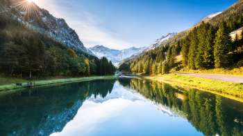 Lac Gänglesee à Steg, entouré de forêts denses et de montagnes enneigées, sous le soleil.