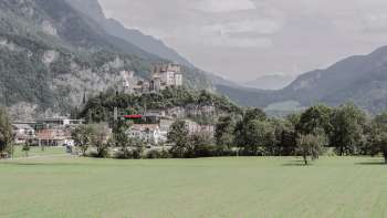 Vue majestueuse sur le château de Gutenberg à Balzers, entouré de champs verdoyants et des impressionnantes Alpes.