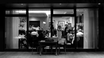 Photo en noir et blanc d'un restaurant animé avec vue de l'extérieur à travers la baie vitrée.