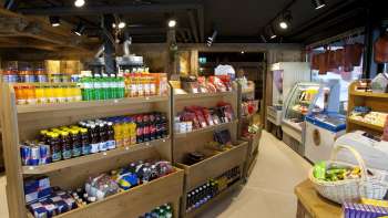 Vue intérieure du Malbuner Läderli avec des étagères en bois remplies de produits régionaux, de boissons et de snacks.