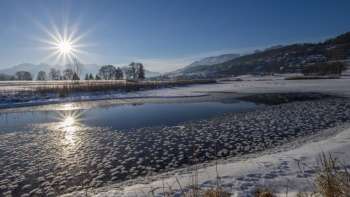 Lever de soleil sur le lac Egelsee à Mauren en hiver avec une surface de glace scintillante, de la neige et un décor de montagne ensoleillé.