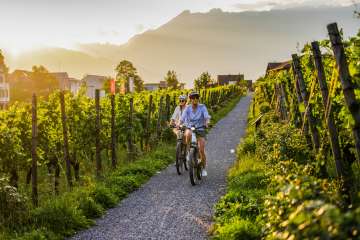 Deux cyclistes dans les vignobles du Liechtenstein au coucher du soleil - vélo électrique avec vue sur les Alpes et les vignes