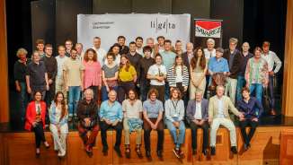 Photo de groupe des participants et des professeurs des Liechtensteiner Gitarrentage (LiGiTa) sur une scène devant une bannière avec le logo de l'événement.