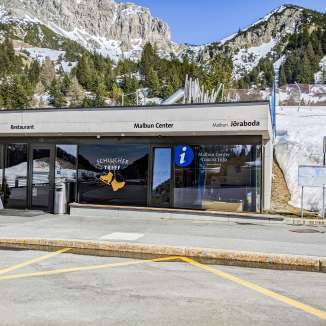 Entrée du Malbun Center avec information touristique et restaurant devant un paysage de montagne enneigé à Malbun, Liechtenstein