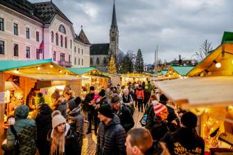 Photo d'ambiance du marché de Noël de Vaduz 2018 avec les stands de fête et la foule devant le bâtiment du gouvernement et la cathédrale.