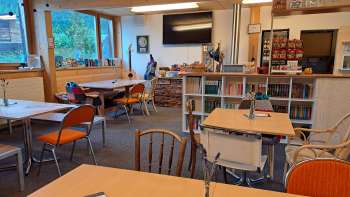 Vue sur la salle de restaurant avec mur en bois et décoration murale - Plusieurs tables avec sièges et vue sur le mur décoratif avec des guitares et des tableaux verts.