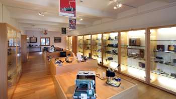 Vue sur une salle d'exposition lumineuse du musée Lawena avec des vitrines éclairées remplies d'appareils électriques historiques.