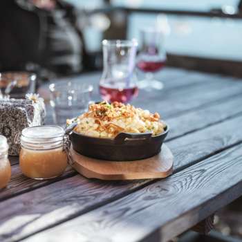Spécialité régionale « Käsknöpfle » avec compote de pommes sur une table en bois devant un décor alpin