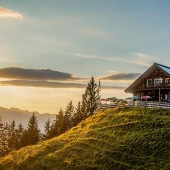 Cabane de Gadafura sur une prairie de montagne ensoleillée avec vue sur les montagnes et le coucher du soleil