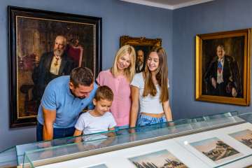 Une famille regarde des objets exposés au Liechtensteinisches Landesmuseum à Vaduz, entourée de peintures et de portraits historiques.