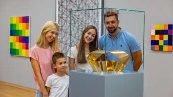 Une famille avec deux enfants regarde une vitrine en verre avec une sculpture en or dans un musée.