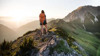 Une randonneuse avec un sac à dos se tient sur une crête de montagne au Liechtenstein et regarde le soleil levant.
