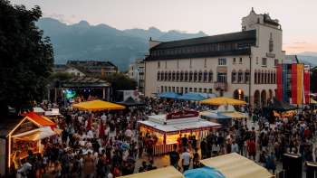 La mairie de Vaduz au crépuscule avec des guirlandes lumineuses, des enfants jouant sur une table de ping-pong et une ambiance estivale le jour de la fête nationale