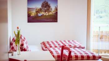 Chambre double confortable dans la maison d'hôtes près du camping Mittagsspitze avec des draps et une décoration à carreaux rouges et blancs.