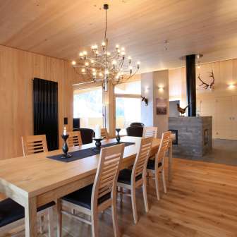 Intérieur en bois clair avec table à manger et cheminée dans la maison Ochsenkopf à Malbun, Liechtenstein