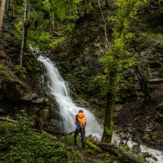 Randonneur avec sac à dos devant une cascade idyllique à Nendeln , niché dans une forêt dense et des rochers couverts de mousse.