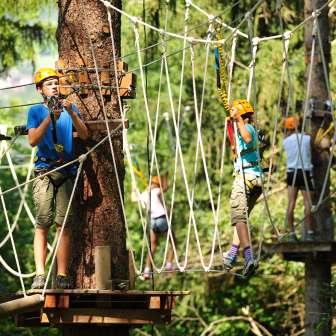 Enfants et adolescents casqués dans le jardin de cordes du parc d'escalade de Triesen au Liechtenstein, assurés sur des éléments d'escalade dans la forêt.