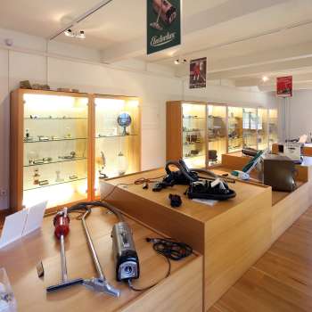 Exposition au Musée Lawena avec des vitrines, de vieux appareils électroménagers et une collection historique d'aspirateurs.
