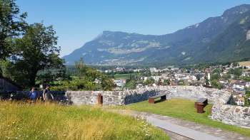 Promenade à travers une allée d'arbres avec vue sur le château de Gutenberg et le décor alpin en arrière-plan