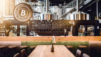 Salle de débit confortable dans la brasserie liechtensteinoise avec tables en bois, installation de tirage et vue sur les cuves de brassage