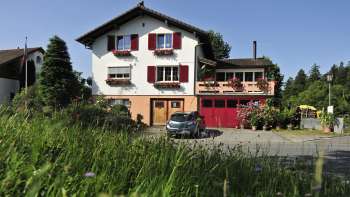 Charmante vue extérieure du Bed & Breakfast Büchel avec des volets rouges et une prairie fleurie au premier plan.