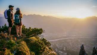 Tina Weirather et Marco Büchel se tiennent au sommet d'une montagne et regardent la vallée du Rhin au Liechtenstein au coucher du soleil.