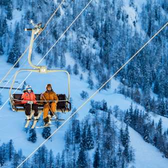 Tina Weirather et Marco Büchel sont assis ensemble sur un télésiège, entourés d'arbres enneigés et d'un paysage hivernal à Malbun.